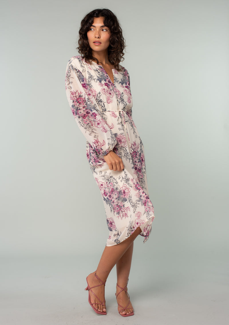 [Color: Natural/Wine] A side facing image of a brunette model wearing a sheer chiffon bohemian mid length dress in a natural and wine pink floral print. With voluminous long sleeves, a split v neckline, and an adjustable drawstring waist. 
