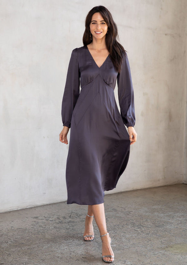 [Color: Gunmetal] A model wearing a dark grey silky maxi dress. With an art deco style paneled skirt, an adjustable strappy back, and voluminous long sleeves.
