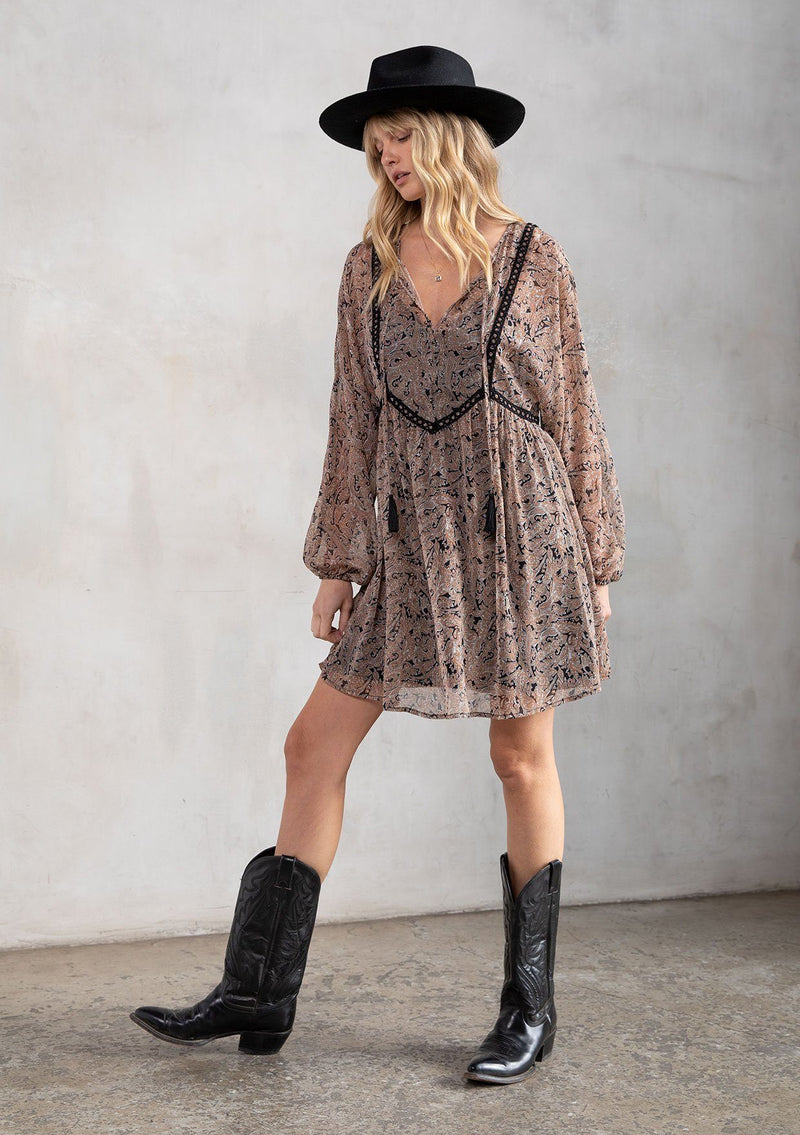 [Color: Black/Coral] A model wearing a dreamy sheer chiffon bohemian black and coral paisley mini dress. With contrast crochet trim, a baby doll dress silhouette, and long sleeves. A flowy Fall bohemian mini dress.