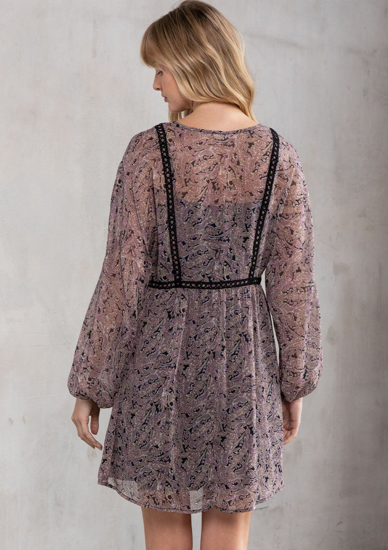 [Color: Black/Orchid] A model wearing a dreamy sheer chiffon bohemian black and purple paisley mini dress. With contrast crochet trim, a baby doll dress silhouette, and long sleeves. A flowy Fall bohemian mini dress.