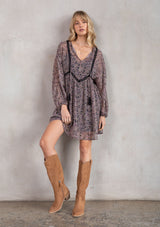 [Color: Black/Orchid] A model wearing a dreamy sheer chiffon bohemian black and purple paisley mini dress. With contrast crochet trim, a baby doll dress silhouette, and long sleeves. A flowy Fall bohemian mini dress.