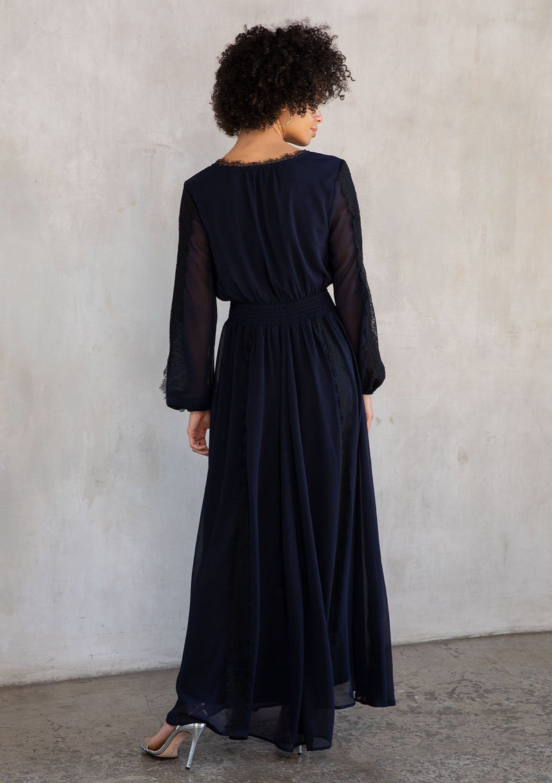 [Color: Navy/Black] A model wearing a dramatic sheer navy chiffon maxi dress with contrast black lace trim details throughout.