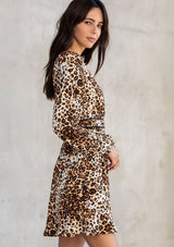 [Color: Camel/Brown] A model wearing a bohemian mini dress in a classic brown leopard print. With long voluminous sleeves, a half smocked elastic waist, contrast trim throughout, a self covered button front, and a v neckline.