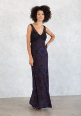 [Color: Black/Cobalt] A model wearing a black and blue paisley print bohemian maxi dress. With a lace overlay top, a v neckline, a side slit, and draped silhouette. 