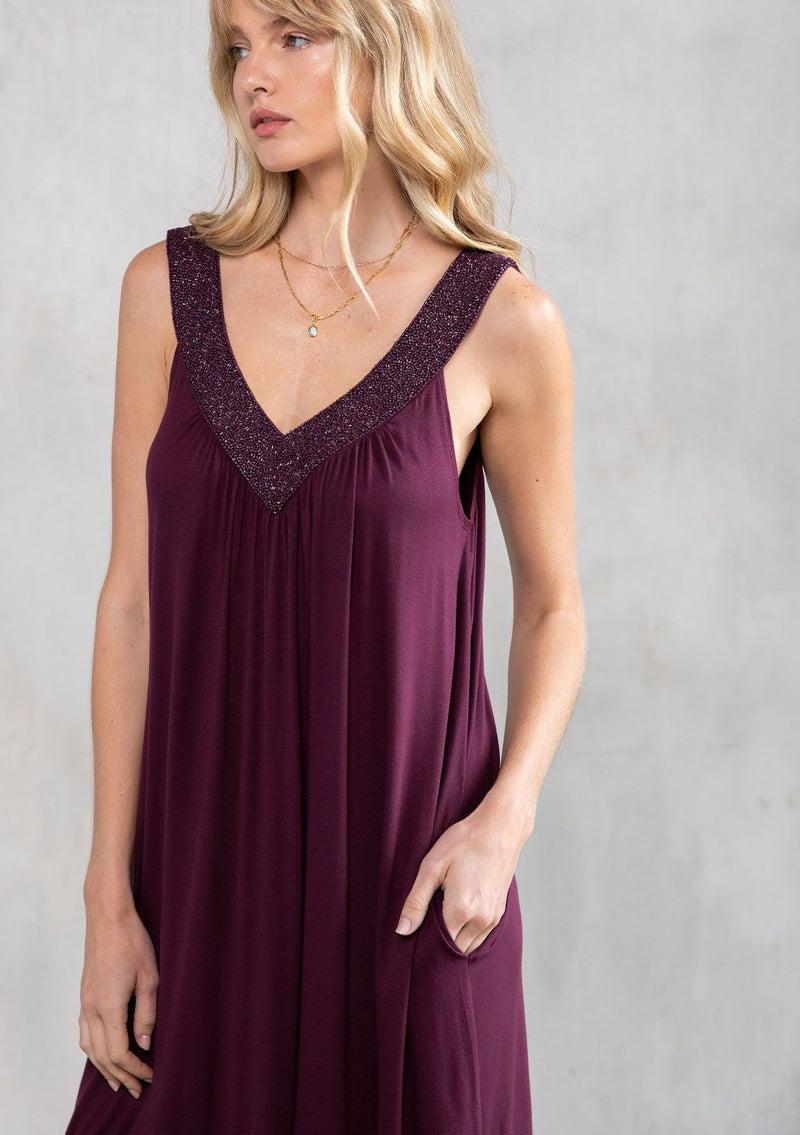 [Color: Fig] A model wearing a purple soft knit, holiday party mini dress with beaded straps, a deep v neckline in front and back, and a flowy swing silhouette. 