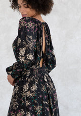 [Color: Black/Jade] A model earing a black and green wildflower print mini dress. With a round neckline and front keyhole detail, an open back with tassel tie closure, a pleated waist detail, and long voluminous sleeves. 