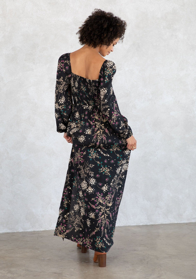 [Color: Black/Jade] A model wearing a bohemian black and green wildflower print maxi dress. With a square neckline, a smocked elastic back, a side slit, and voluminous long sleeves. 