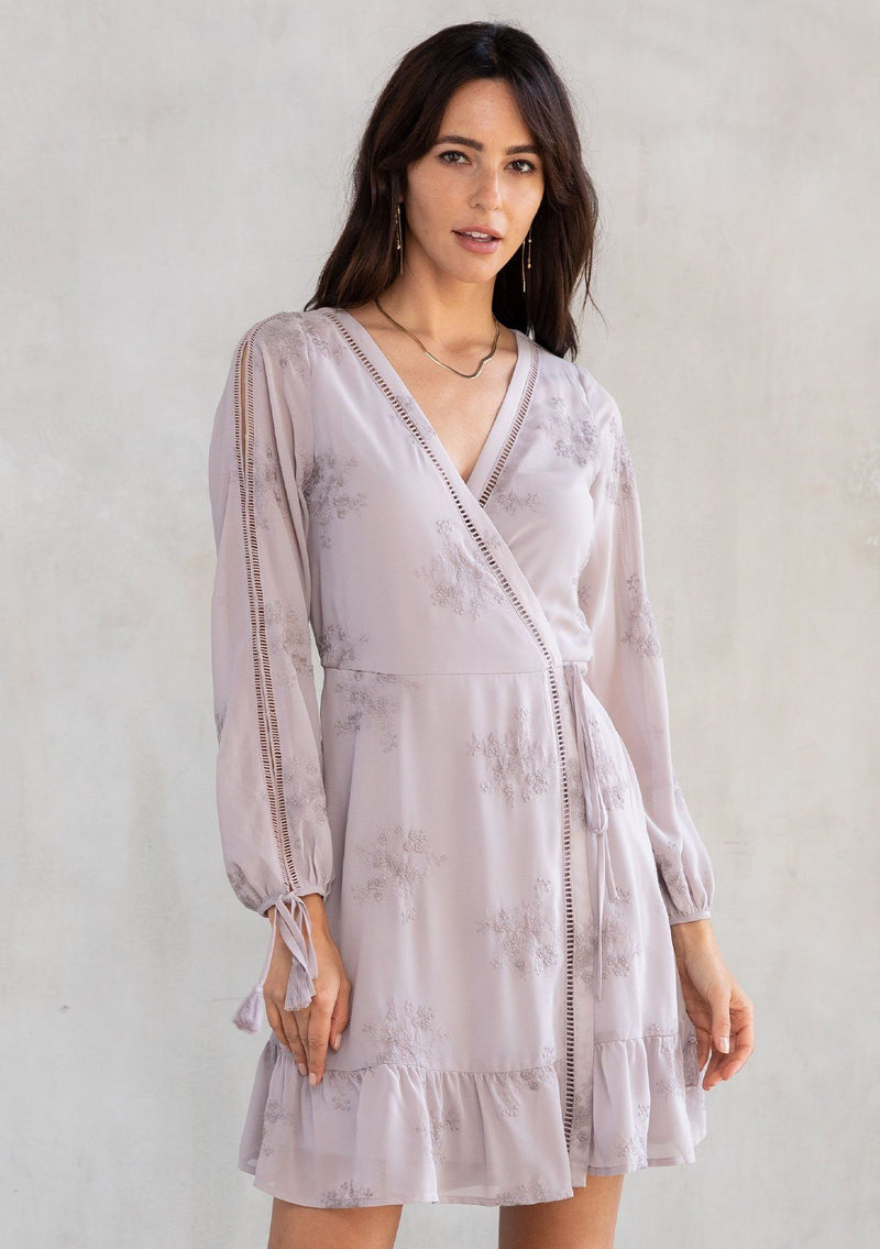 [Color: Dusty Mauve] A model wearing a charming light purple embroidered chiffon mini wrap dress, with sheer long split sleeves, lattice trim details, and a wrap front with side tie closure. 