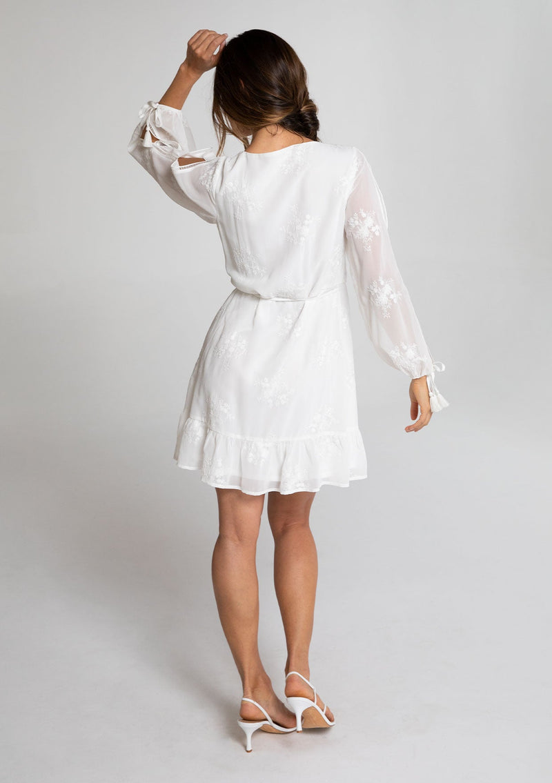 [Color: White] A model wearing a charming white embroidered chiffon mini wrap dress, with sheer long split sleeves, lattice trim details, and a wrap front with side tie closure.