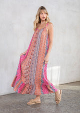 [Color: Coral Multi] A model wearing a vacation ready sleeveless maxi dress in a multicolor mixed print. With a ruffled round neckline, a relaxed flowy fit, and metallic thread details.