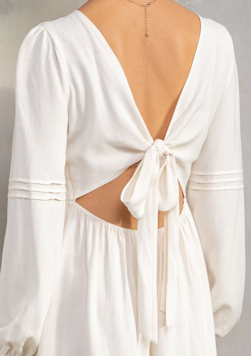 [Color: Vanilla] A model wearing a classic off white bohemian mini dress in a linen blend. With long voluminous sleeves, a tie back detail, and open back detail. 