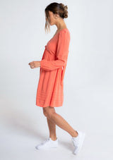 [Color: Papaya] A model wearing a classic coral bohemian mini dress in a linen blend. With long voluminous sleeves, a tie back detail, and open back detail.