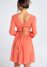 [Color: Papaya] A model wearing a classic coral bohemian mini dress in a linen blend. With long voluminous sleeves, a tie back detail, and open back detail.