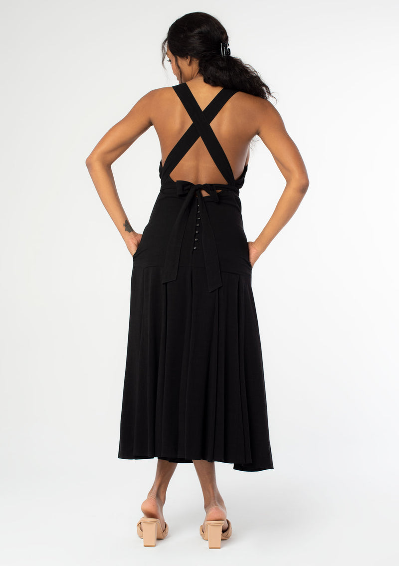 [Color: Black] A back facing image of a black model wearing a sleeveless black halter maxi dress. A linen blend tank dress with a sexy open back, cross back racer back straps, side pockets, and a back button detail. 