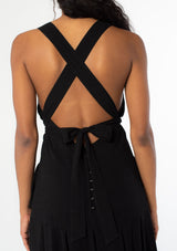 [Color: Black] A close up back facing image of a black model wearing a sleeveless black halter maxi dress. A linen blend tank dress with a sexy open back, cross back racer back straps, side pockets, and a back button detail. 