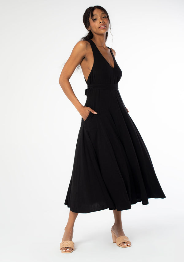 [Color: Black] A front facing image of a black model wearing a sleeveless black halter maxi dress. A linen blend tank dress with a sexy open back, cross back racer back straps, side pockets, and a back button detail. 