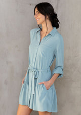 [Color: Dusty Teal] A model wearing a pretty light teal linen blend mini shirtdress. With a flowy tiered skirt, a button front, and long rolled sleeves. 
