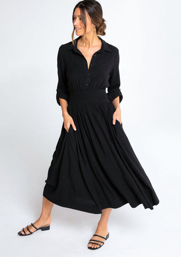 [Color: Black] A model wearing a simple, elevated black mid length shirt dress in a linen blend fabric. 