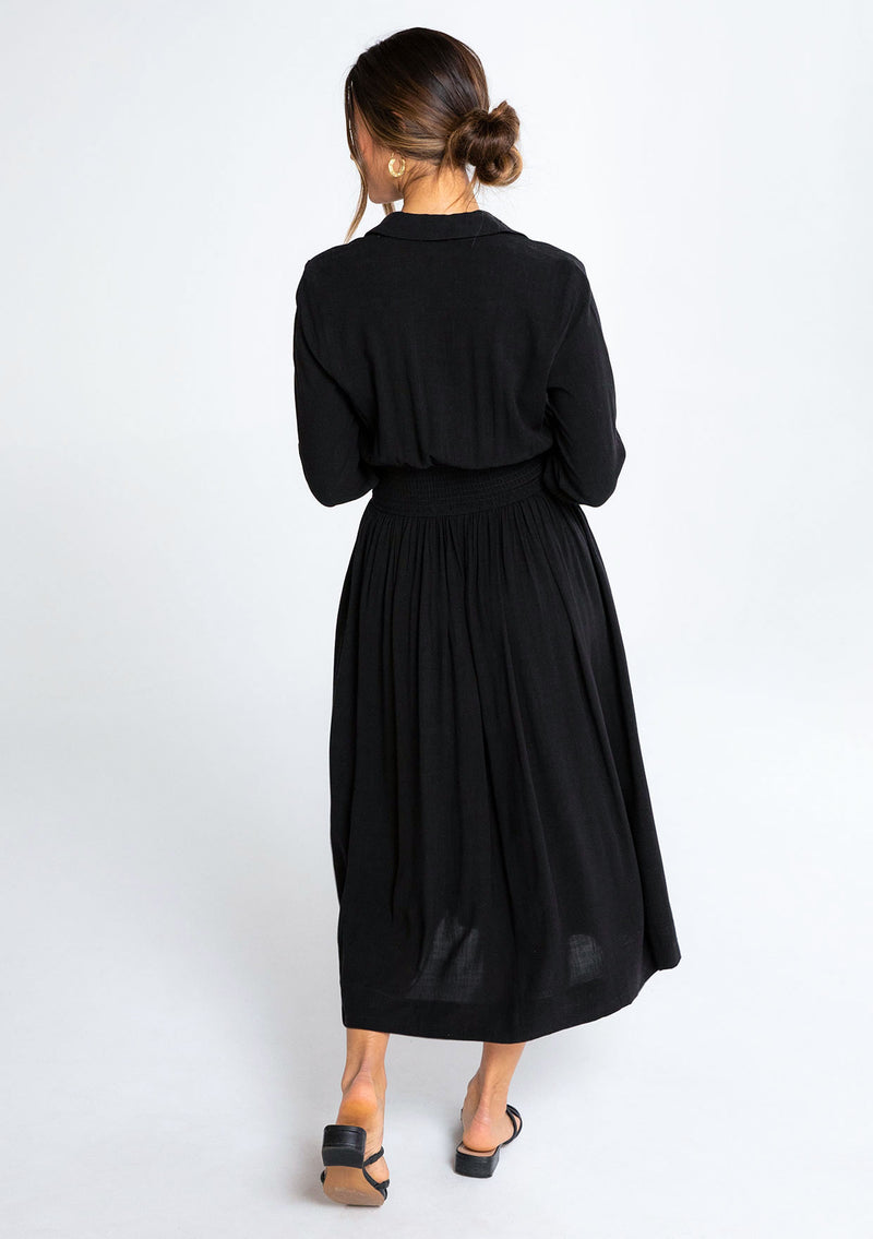 [Color: Black] A model wearing a simple, elevated black mid length shirt dress in a linen blend fabric. 