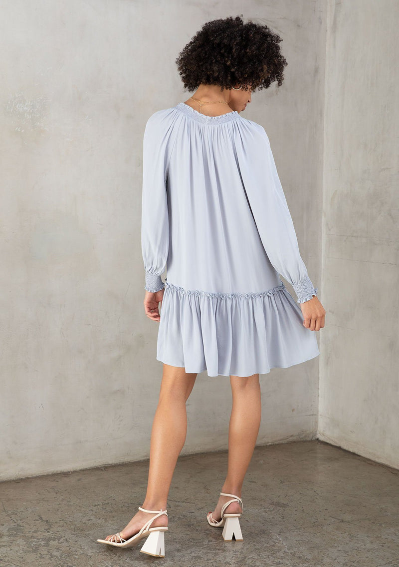 [Color: Powder Blue] A model wearing a classic light blue bohemian mini dress in a silky crepe. With a ruffled tiered skirt, flowy silhouette, and voluminous long sleeves.