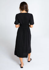 [Color: Black] A model wearing a timeless black linen blend maxi dress. With short puff sleeves, a flattering pleated waist, and delicate lattice trim.