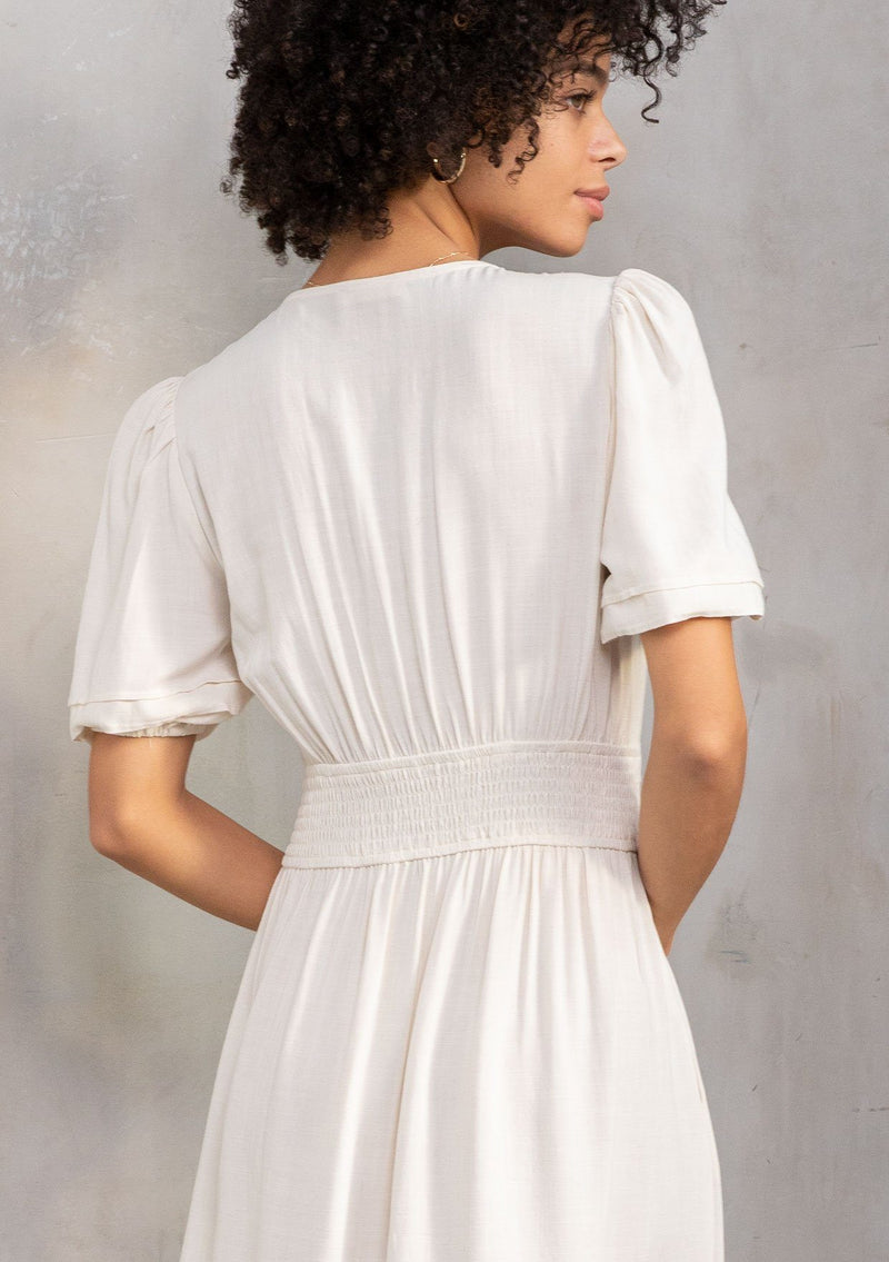 [Color: Vanilla] A model wearing a timeless off white linen blend maxi dress. With short puff sleeves, a flattering pleated waist, and delicate lattice trim. 