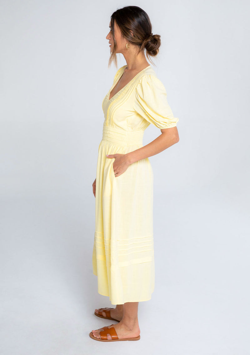 [Color: Daffodil] A model wearing a timeless yellow linen blend maxi dress. With short puff sleeves, a flattering pleated waist, and delicate lattice trim.