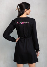 [Color: Black/Mulberry] A model wearing a black mini wrap dress with pink floral embroidery. 