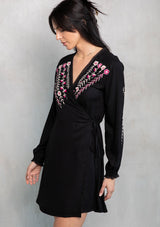 [Color: Black/Mulberry] A model wearing a black mini wrap dress with pink floral embroidery. 