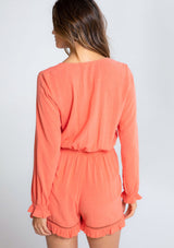 [Color: Papaya] A model wearing a coral ruffled long sleeve short romper made from a linen blend. With a tie front waist detail. 