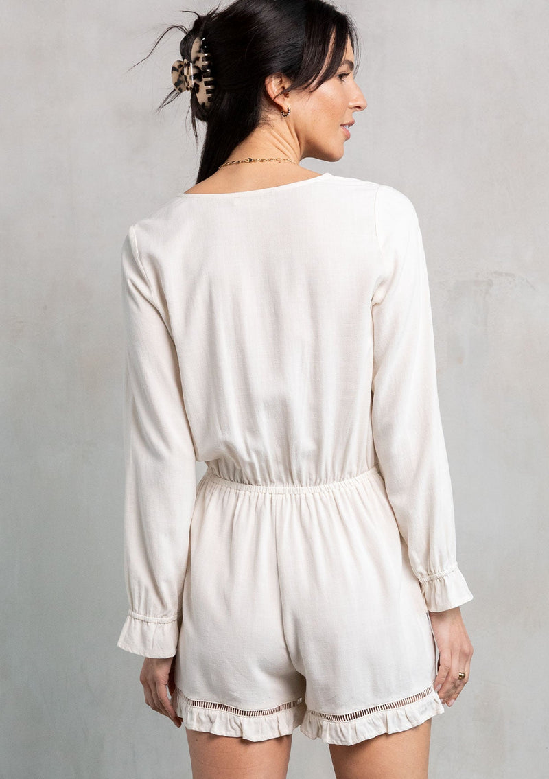 [Color: Vanilla] A model wearing an off white ruffled long sleeve short romper made from a linen blend. With a tie front waist detail. 