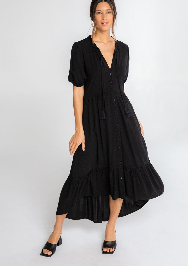 [Color: Black] A model wearing a black flowy bohemian mid length dress with a button front and short puff sleeves. 