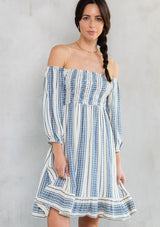 [Color: Natural/Indigo] A model wearing an off white smocked mini dress with an indigo yarn dye stripe. 
