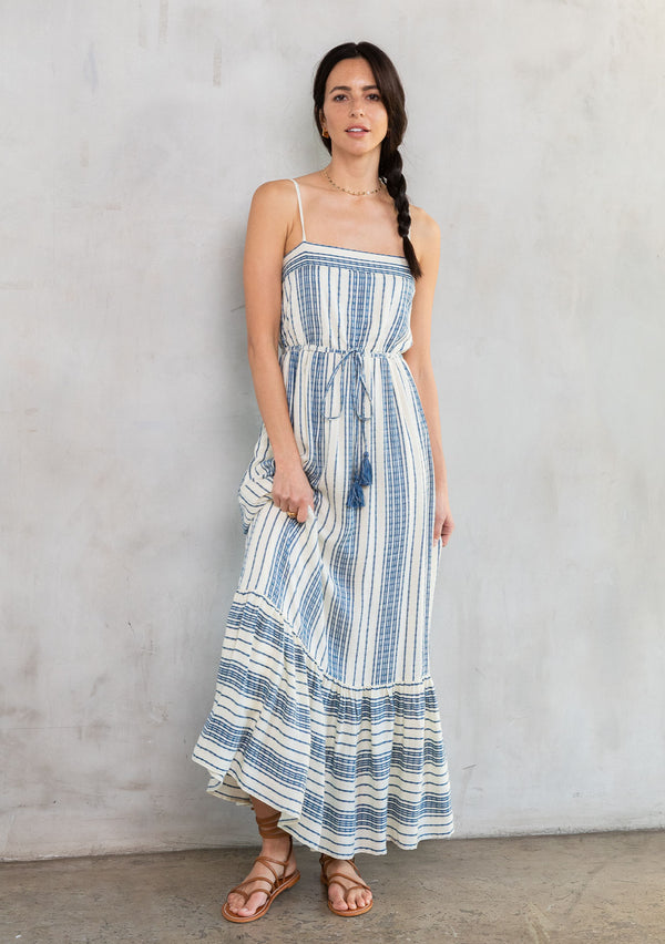 [Color: Natural/Indigo] A model wearing a flowy sleeveless beach maxi dress in a natural and indigo blue stripe. 