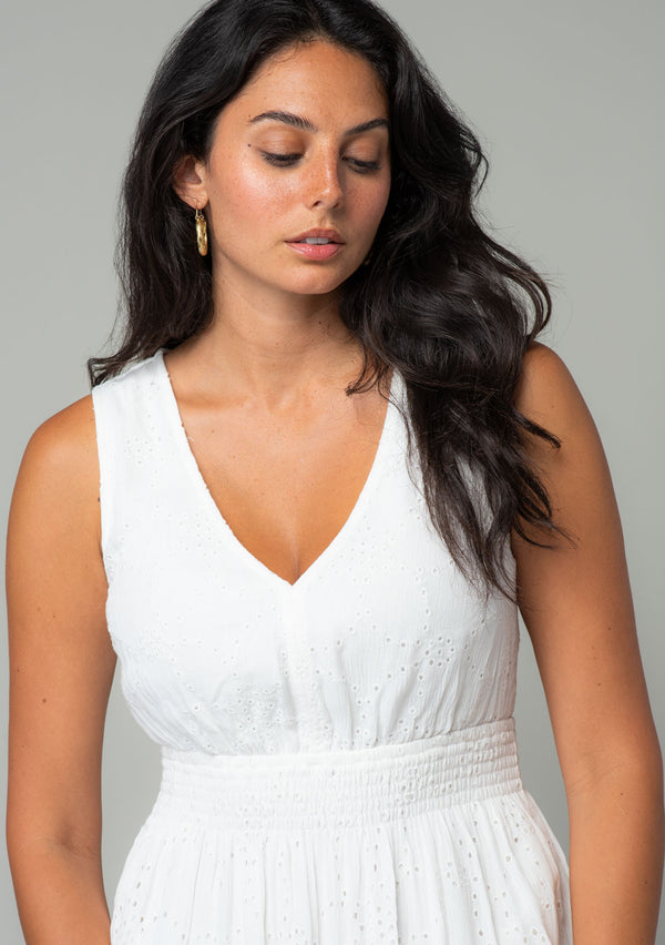 [Color: Off White] A close up front facing image of a brunette model wearing a sleeveless white bohemian eyelet maxi dress. With a v neckline, a long tiered skirt, and a smocked elastic waist. A classic bohemian white maxi dress for Summer. 