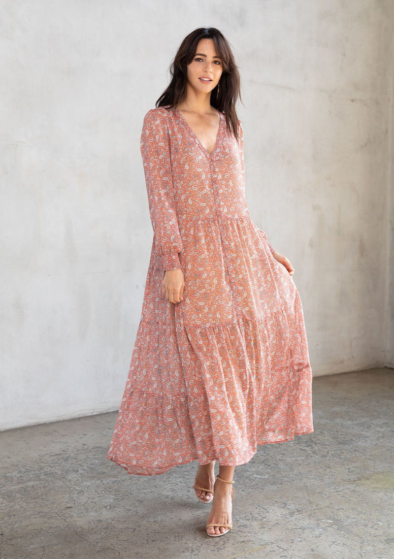 [Color: Coral/Natural] A model wearing an ethereal maxi dress in sheer chiffon, designed in a bohemian coral paisley print. With gold lurex details, long sleeves, and a button front. 