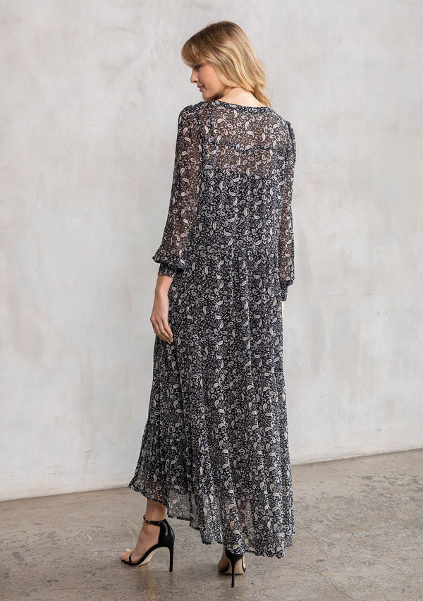 [Color: Black/Natural] A model wearing an ethereal maxi dress in sheer chiffon, designed in a bohemian black paisley print. With gold lurex details, long sleeves, and a button front. 