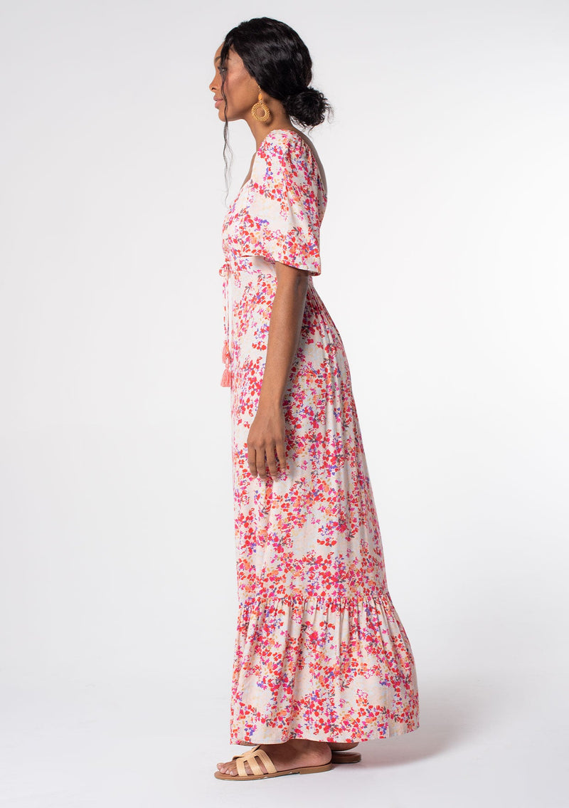 [Color: Blush/Red] A model wearing a romantic pink and red floral print maxi dress with short flutter sleeves, a gathered sweetheart neckline, and tassel accents. A bohemian maxi dress for Spring and Summer. 