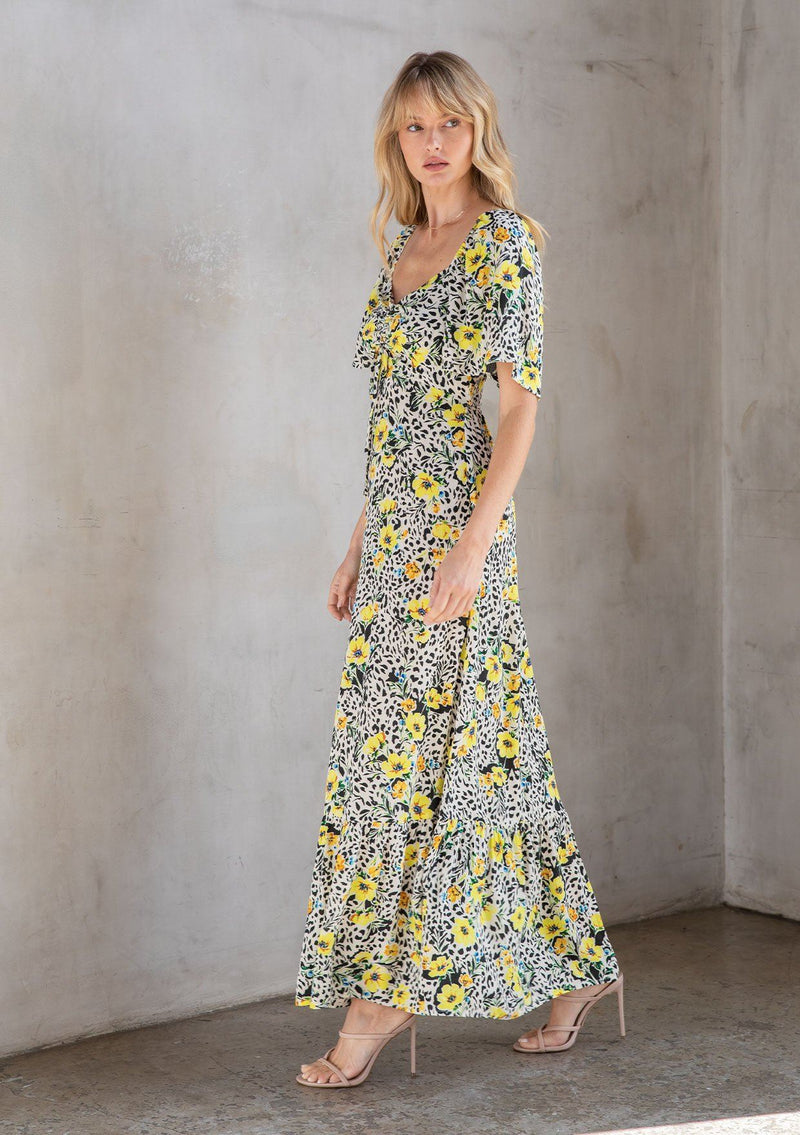 [Color: Ivory/Lemon] A model wearing an effortlessly pretty bohemian resort maxi dress in a yellow floral print. With a gathered tie front neckline and a smocked bodice at the back.
