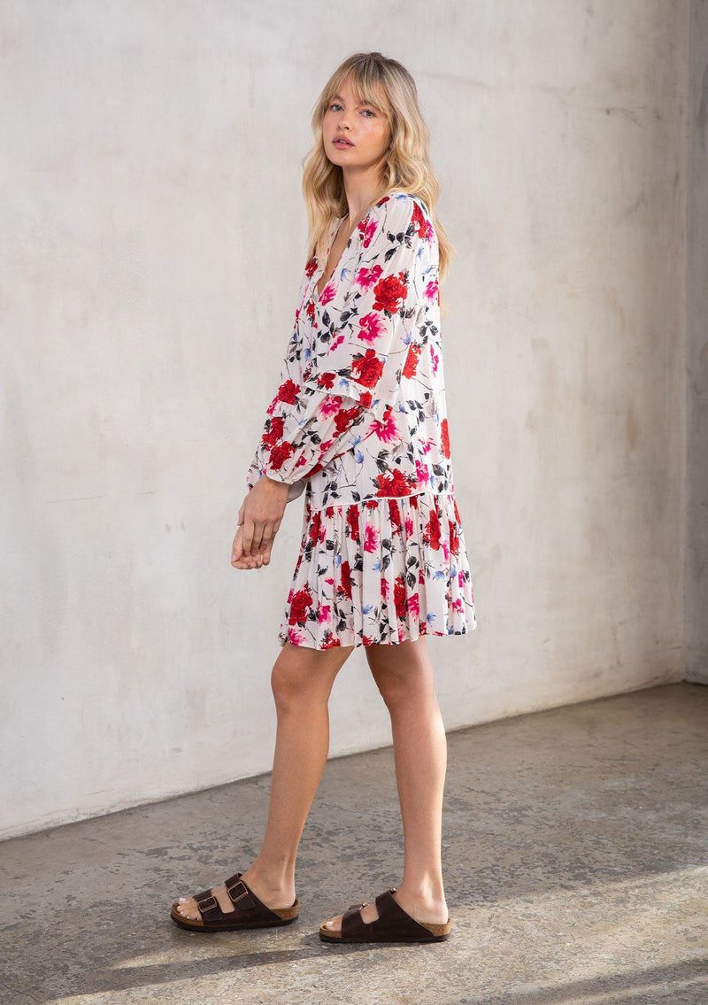 [Color: Cream/Red] A model wearing a charming Spring baby doll mini dress in a red rose floral print. With long ruffled sleeves, a self covered button front, and a drop waist. 