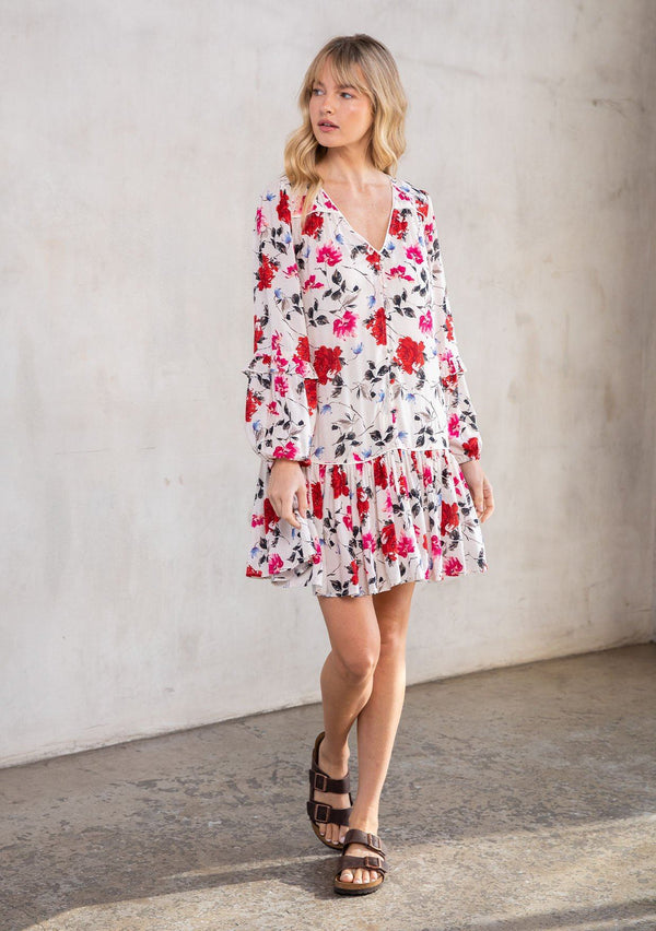 [Color: Cream/Red] A model wearing a charming Spring baby doll mini dress in a red rose floral print. With long ruffled sleeves, a self covered button front, and a drop waist. 