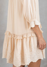 [Color: Natural] A model wearing a classic natural bohemian mini dress with a ruffle trimmed tiered skirt, button front, and embroidered detail throughout. 