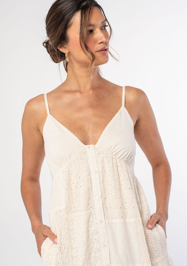 [Color: Natural] A woman wearing an off white bohemian cotton tank maxi dress with patchwork embroidery and dobby. With spaghetti straps and a button front. 