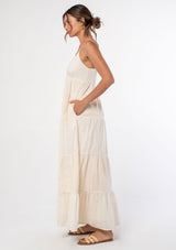 [Color: Natural] A woman wearing an off white bohemian cotton tank maxi dress with patchwork embroidery and dobby. With spaghetti straps and a button front. 