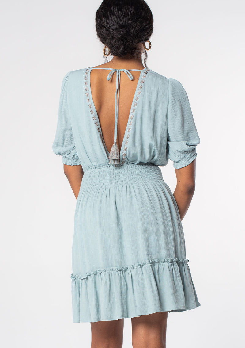 [Color: Seafoam/Taupe] A model wearing a seafoam green linen blend spring mini dress with bohemian embroidered front, an open back, and flowy skirt. 