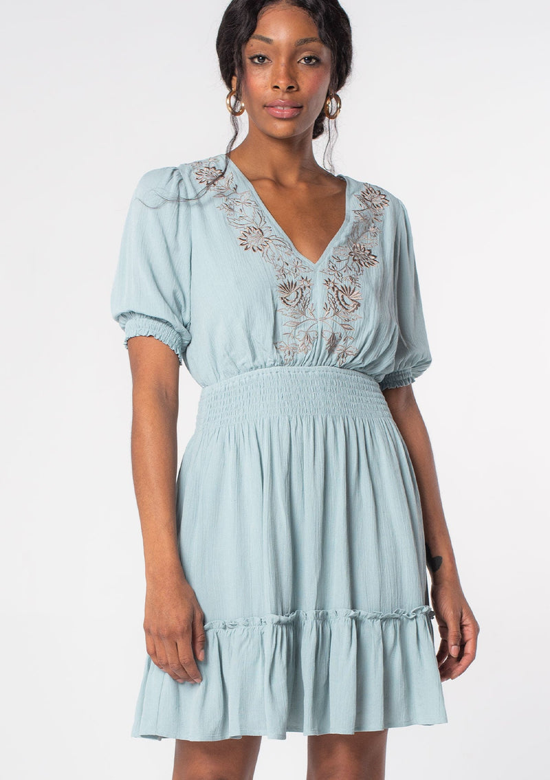 [Color: Seafoam/Taupe] A model wearing a seafoam green linen blend spring mini dress with bohemian embroidered front, an open back, and flowy skirt. 