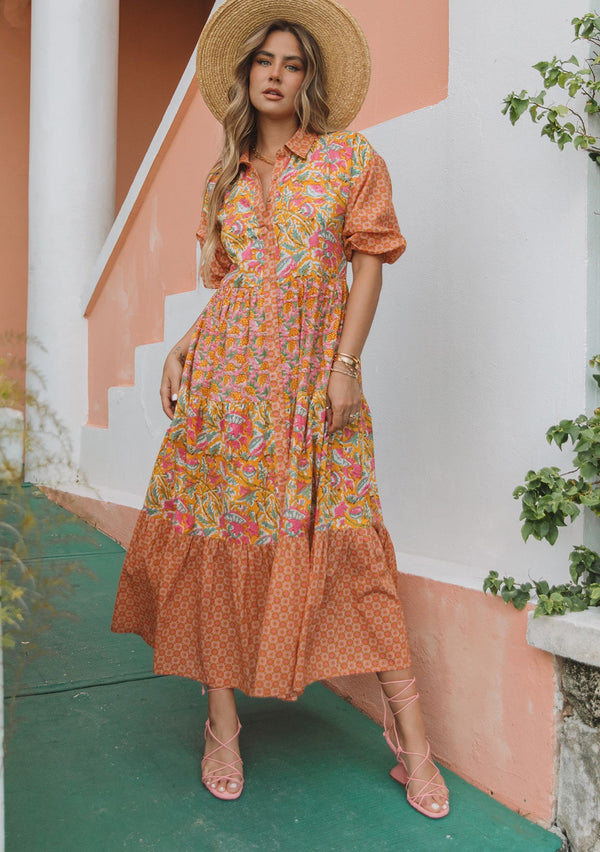 [Color: Pink/Mango] A woman wearing a flowy cotton bohemian maxi dress in a bright pink and yellow mixed floral print. With half length puff sleeves, a collared neckline and a button front.