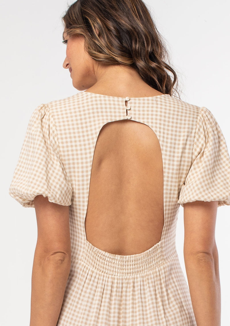 [Color: Tan/Natural] A model wearing a tan and white small checkered gingham mid length dress with short puff sleeves and an open back detail with button closure.