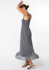 [Color: Black/Off White] A model wearing a black and white gingham checkered maxi dress in a clip dot chiffon. With ruffled tank top straps, a smocked bodice, and a square neckline. 