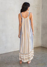 [Color: Dijon/Navy] A model wearing a vacation ready sleeveless maxi dress in a yellow and blue stripe. With a ruffled round neckline, a relaxed flowy fit, and a tiered skirt. 